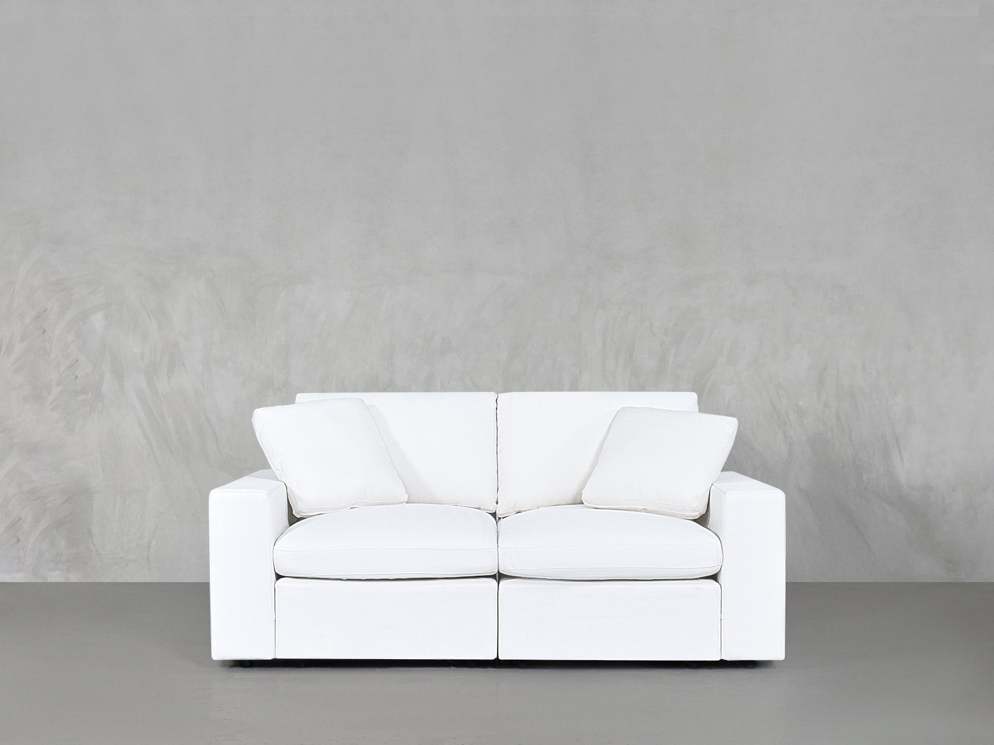 Two-seater white sofa with cushions against grey wall