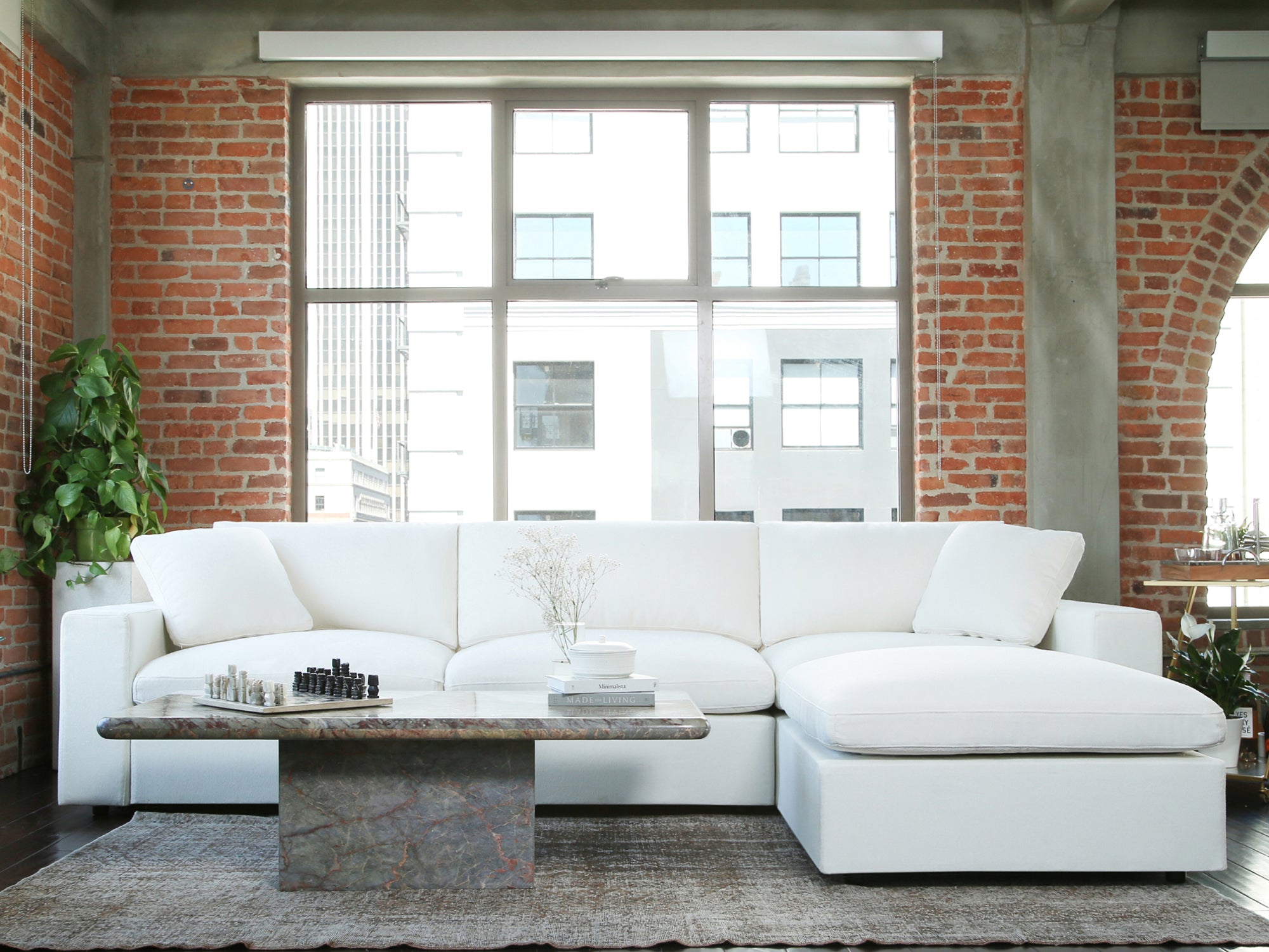 Living room scene with white sectional couch and brick wall window backdrop